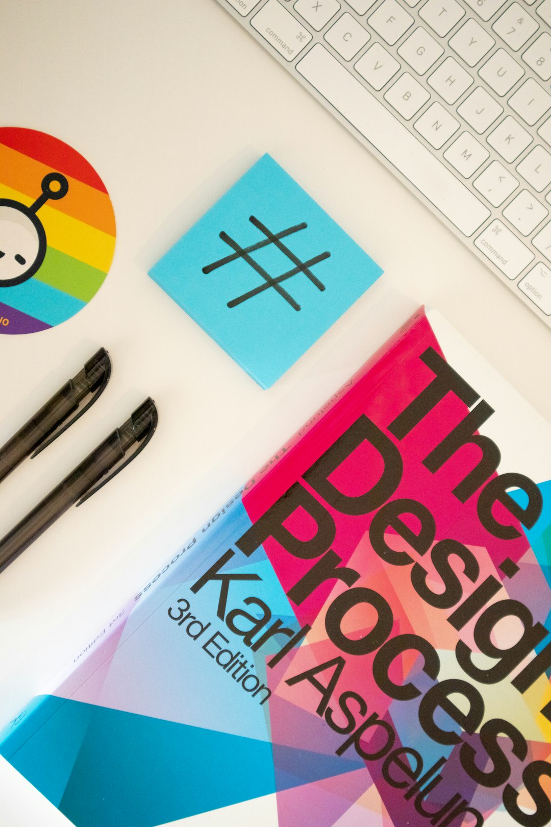 Home desk with a design book, stationary elements and a sticky note with a hashtag on it